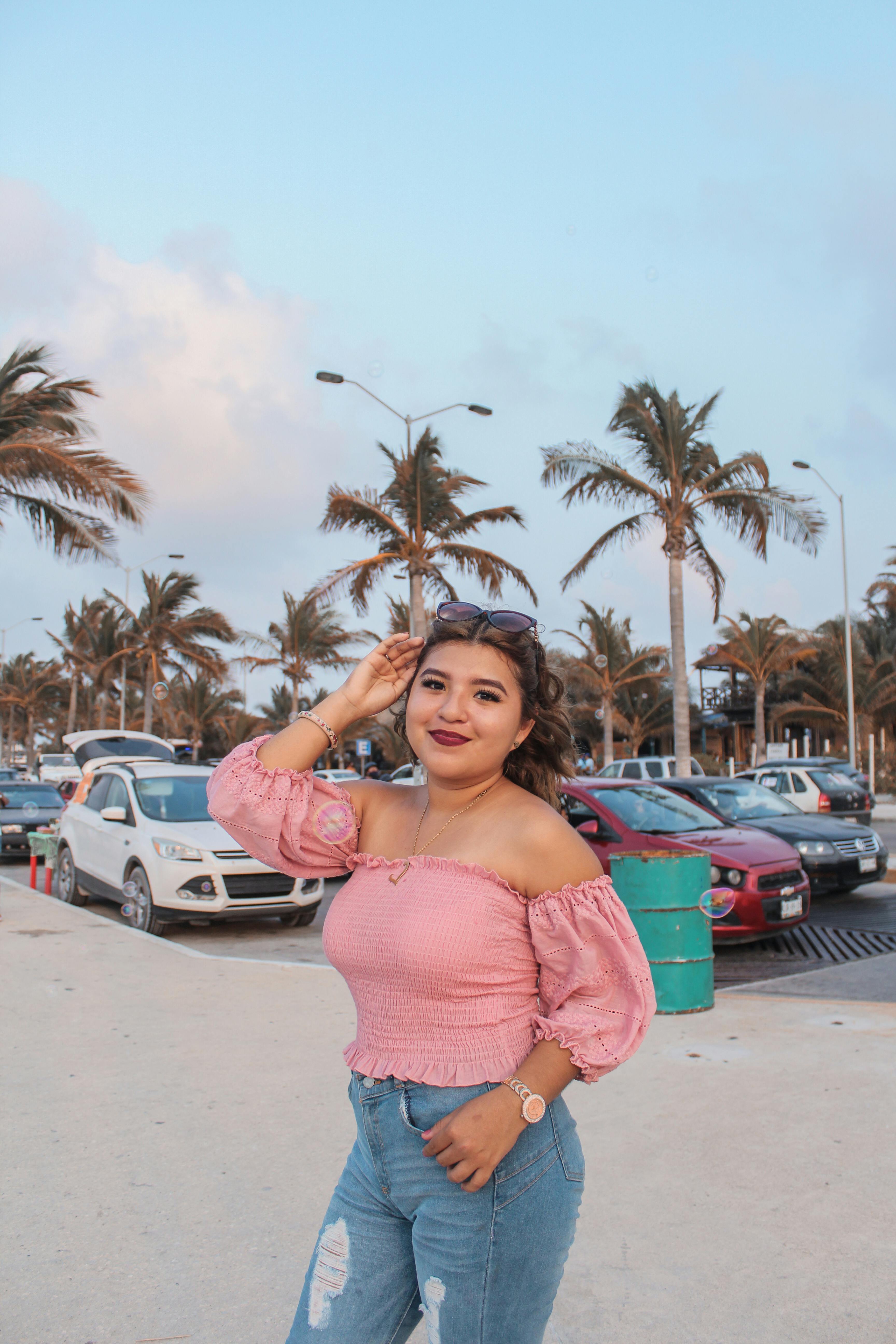 beautiful woman in a pink top standing near a parking lot