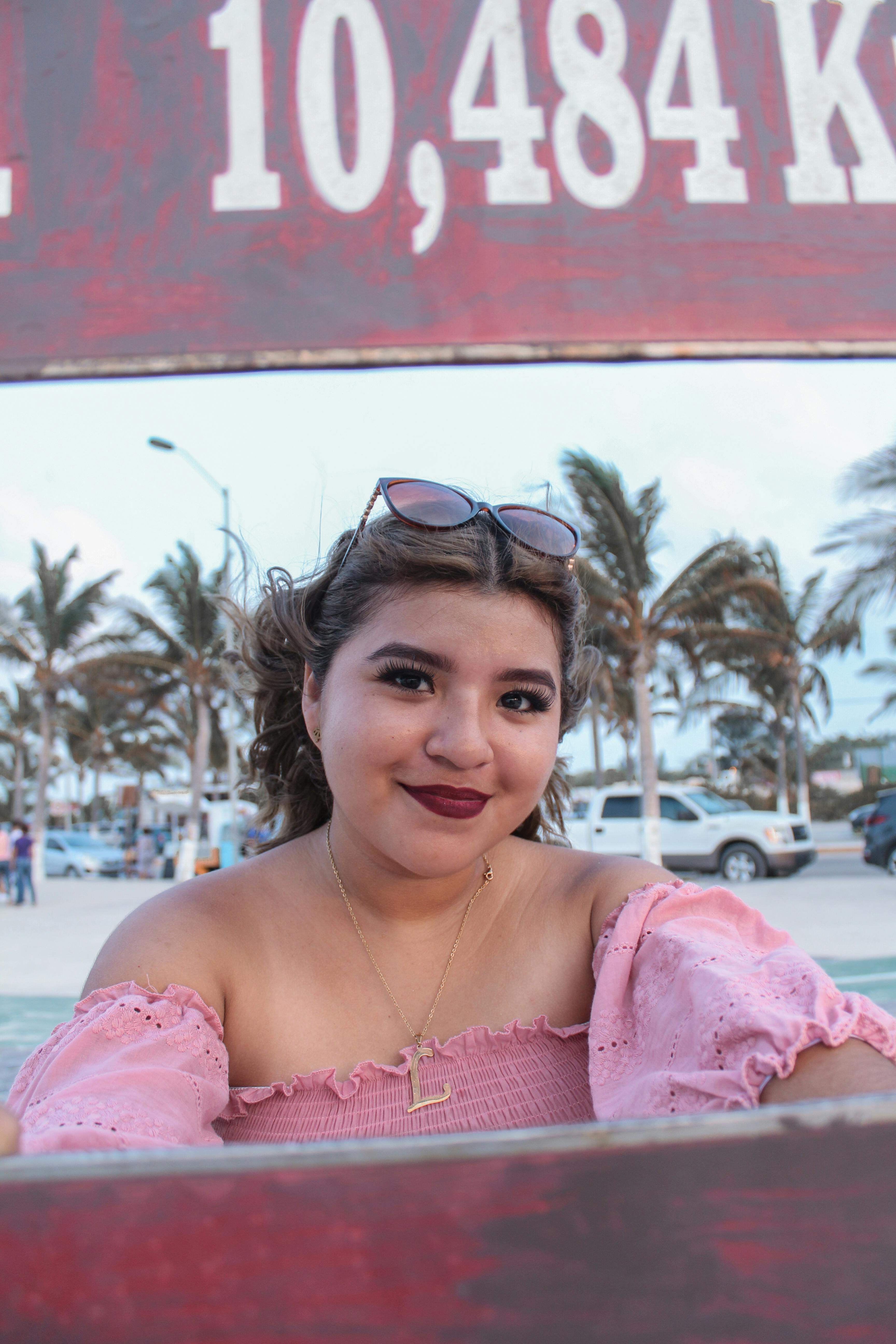 A young woman with a bright smile and stylish attire enjoying a sunny day at the beach.