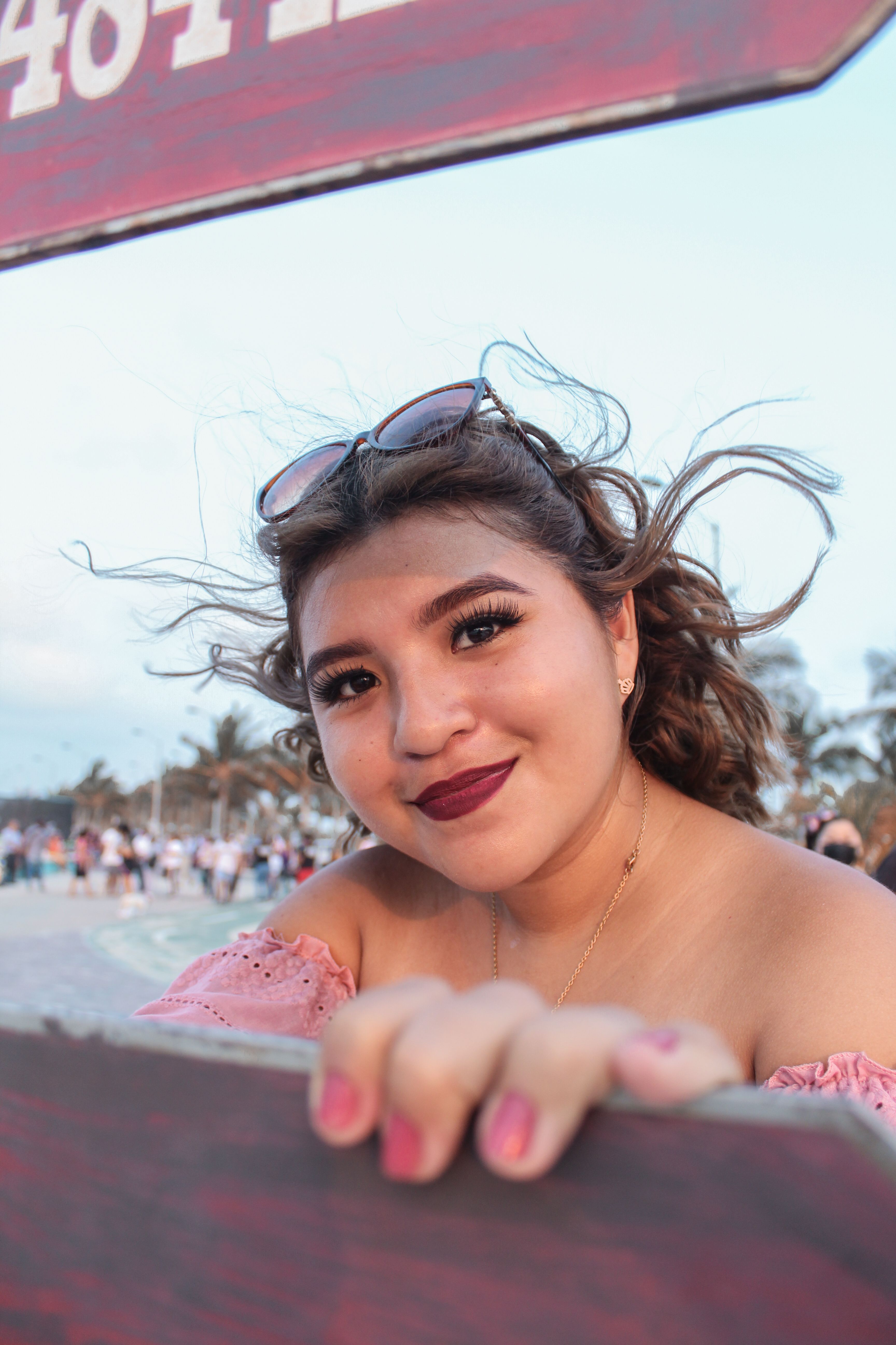 Close-up of a smiling woman with wavy hair and sunglasses at a beach during the day.