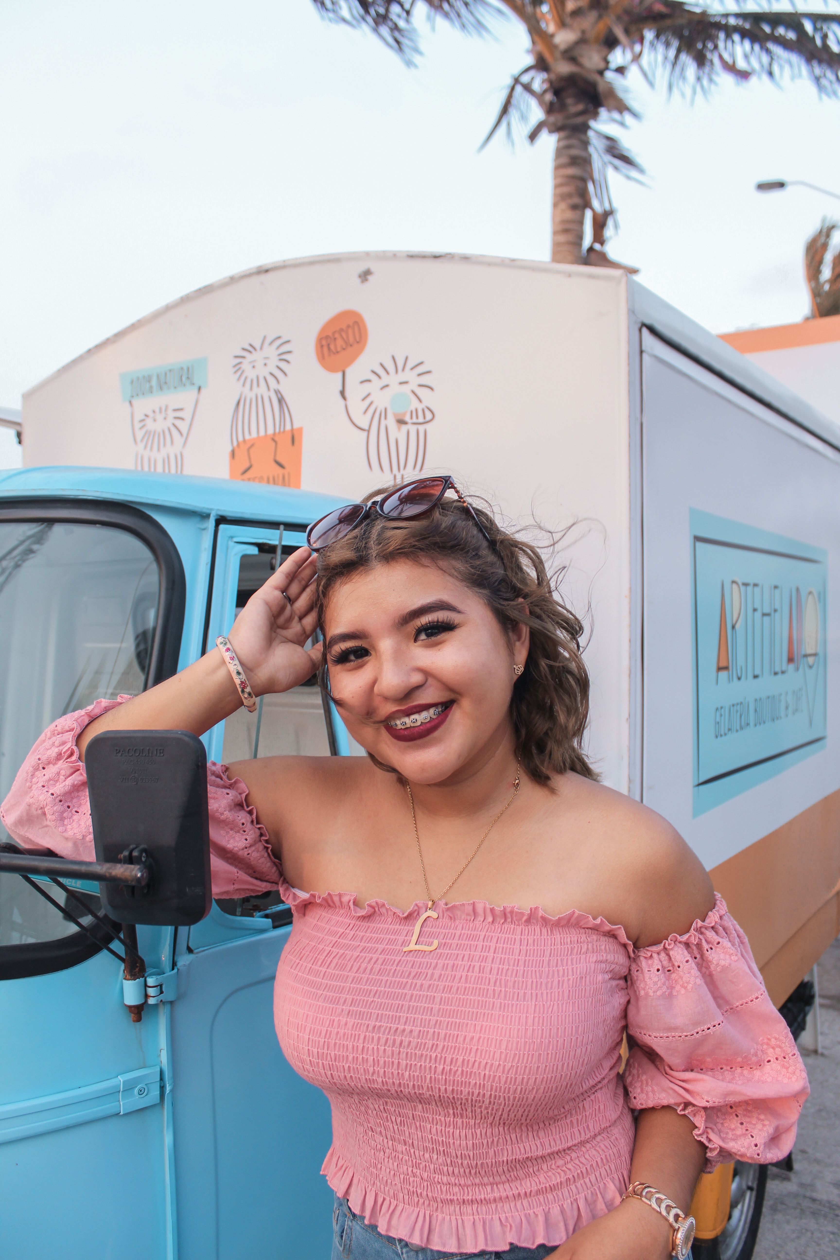 A young woman in a pink top poses happily outdoors near a colorful van.