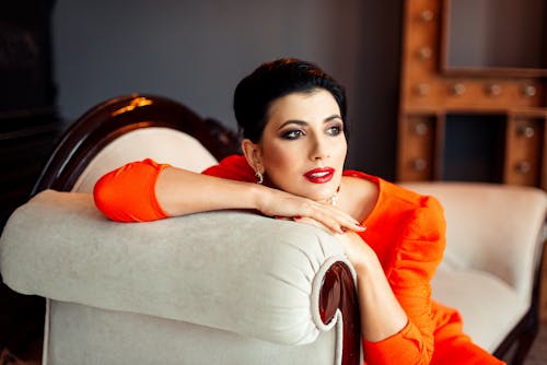 Pensive female with bright makeup looking away while resting on comfortable white armchair