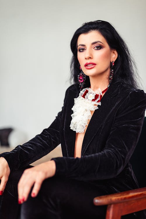 Free Confident woman with dark hair in stylish clothes sitting on chair and looking at camera in light room Stock Photo