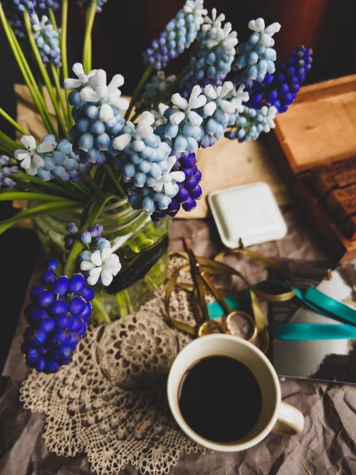 Free A charming flat lay featuring a cup of coffee, vibrant blue hyacinths, and decorative elements on a rustic table. Stock Photo
