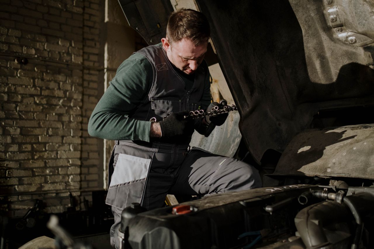 Mechaniker kontrolliert Bauteile im Motorraum unter Werkstattlicht.