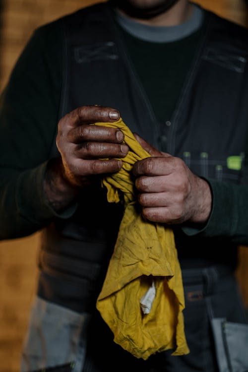 Crop anonymous male mechanic in uniform wiping greased hands while standing in repair workshop