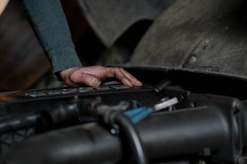 Crop unrecognizable male technician with dirty hands checking motor of vehicle in repairing workshop