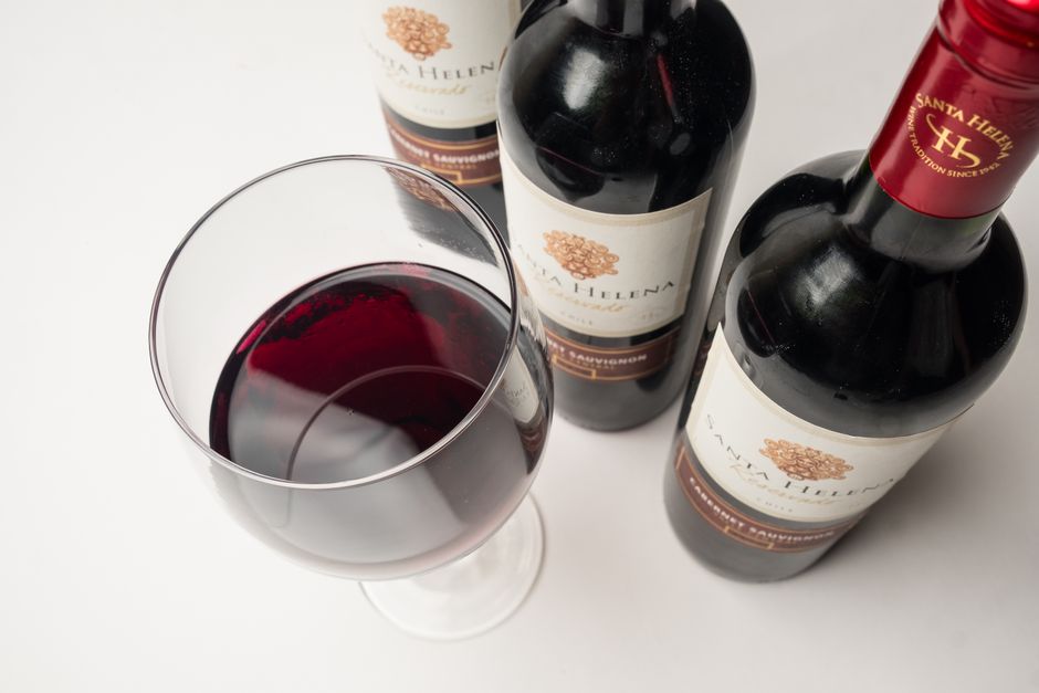 Close-up of red wine glass with Santa Helena wine bottles on a white background.