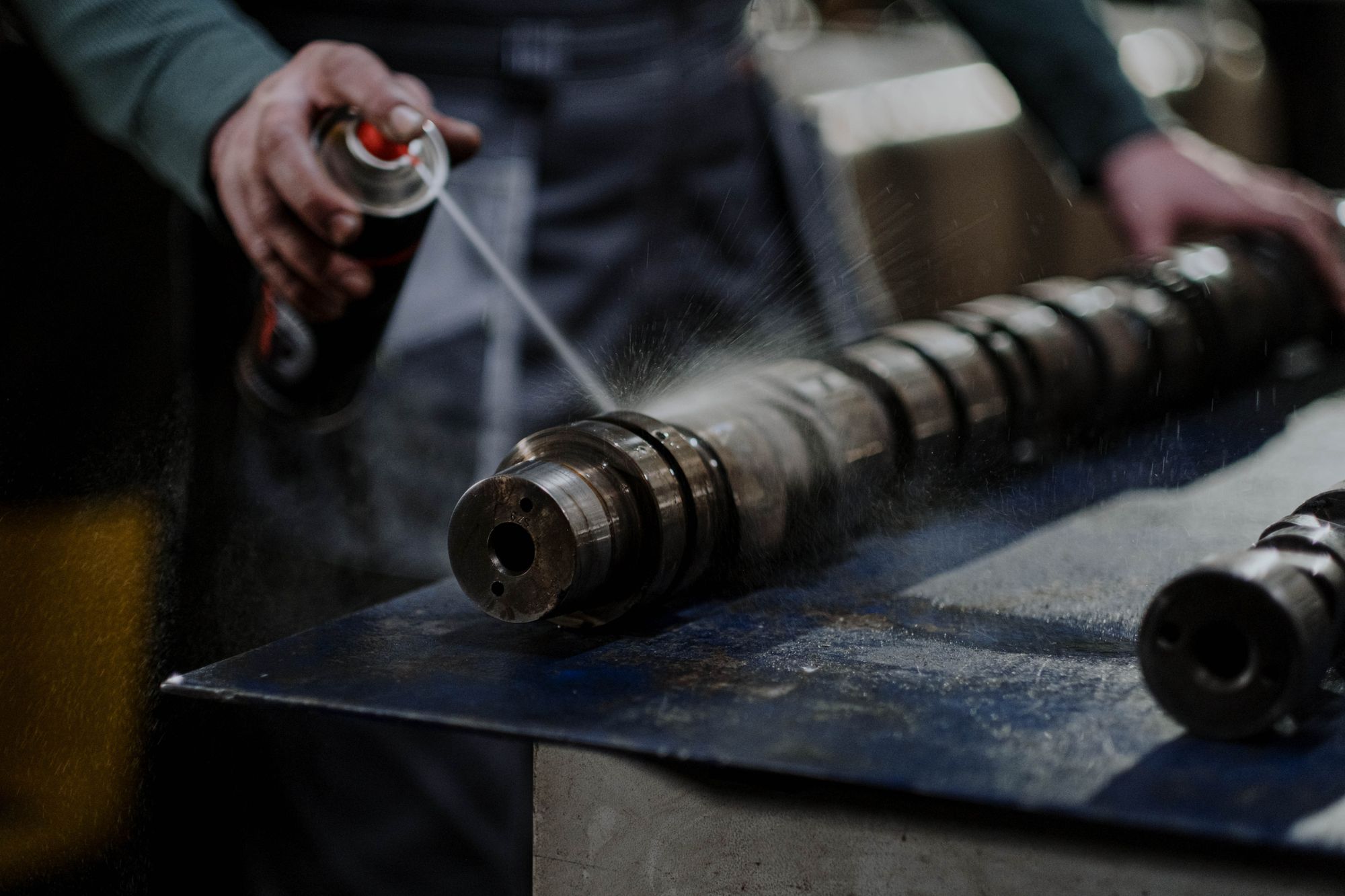 Shows a worker spraying something onto an engine part, closely matching the article