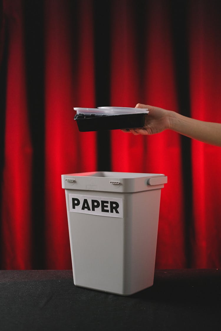 Person Putting Plastic Into A Paper Wastebasket