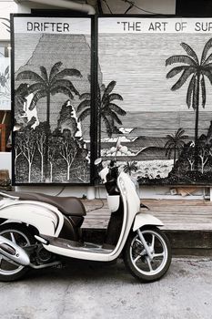 Vintage scooter parked in front of a surf-themed mural featuring palm trees and the ocean.