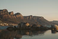Person Standing on Brown Rock Formation Near Body of Water
