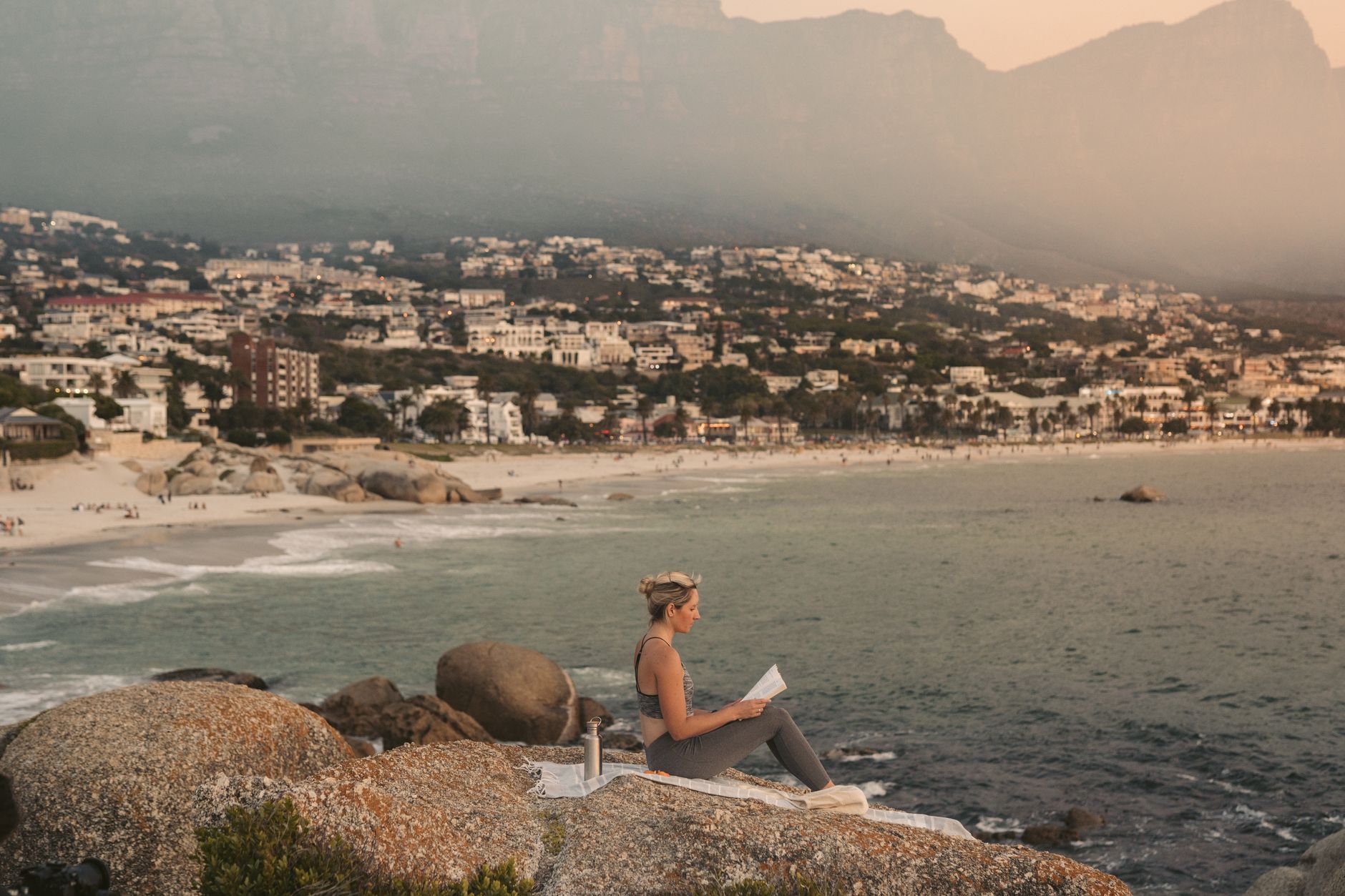 Woman reading on the rocks overlooking the coastline in Cape Town, South Africa during sunset.