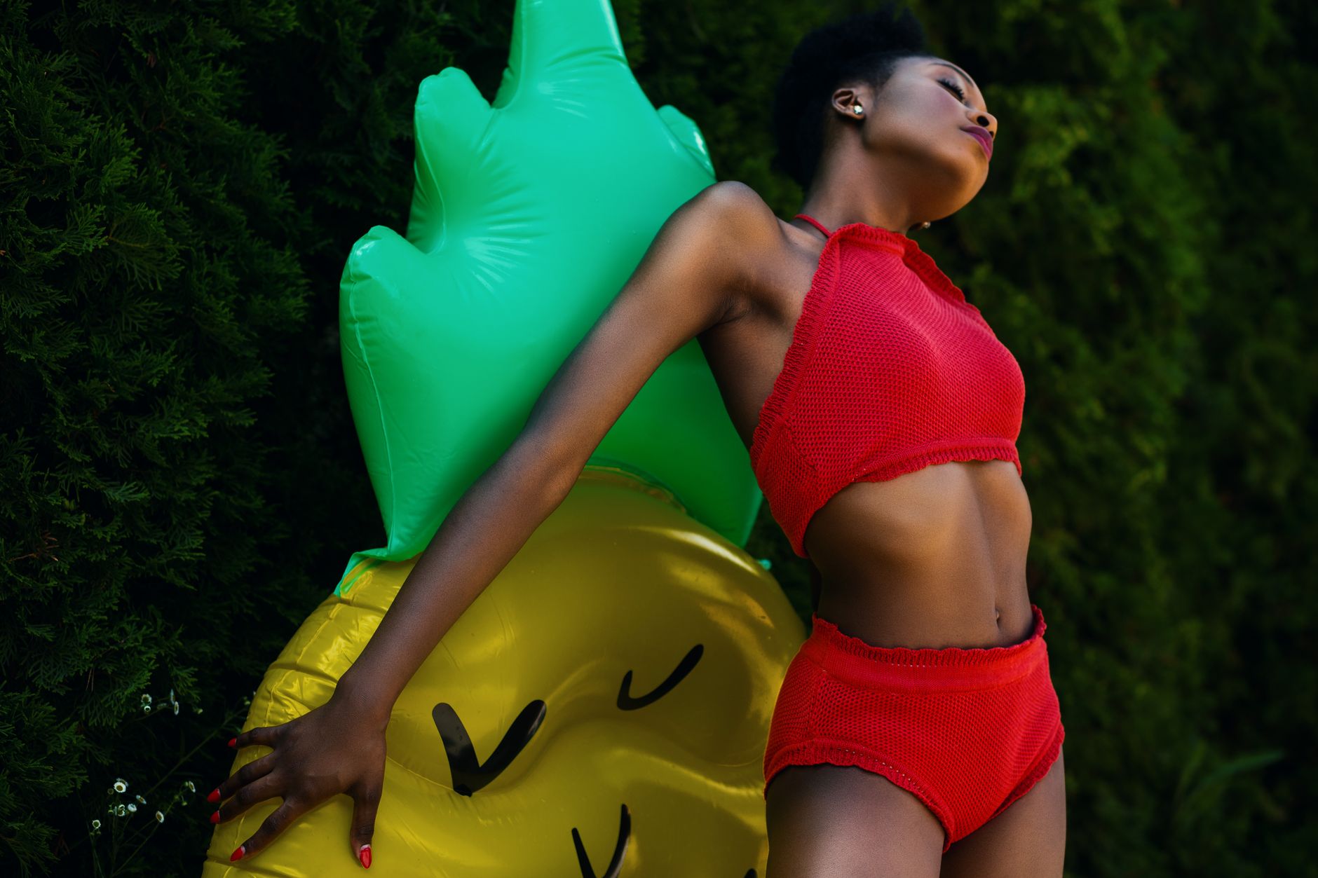 Stylish outdoor photoshoot with a woman in red swimwear and inflatable pineapple.