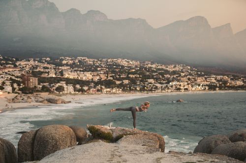 Free Woman practicing yoga on Cape Town's scenic coastline with mountain backdrop. Stock Photo