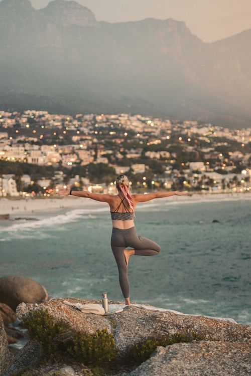 Free A woman practices yoga by the ocean, overlooking Cape Town's coastline at sunset. Stock Photo