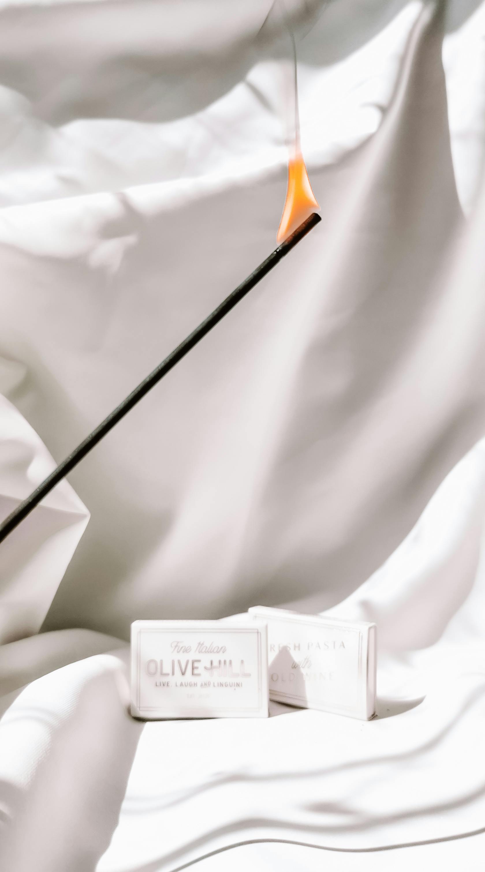 A burning incense stick with flame against draped fabric background, creating a serene ambiance.
