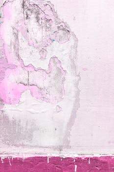 An abstract view of an aging concrete wall with peeling pink paint creating a rough texture.