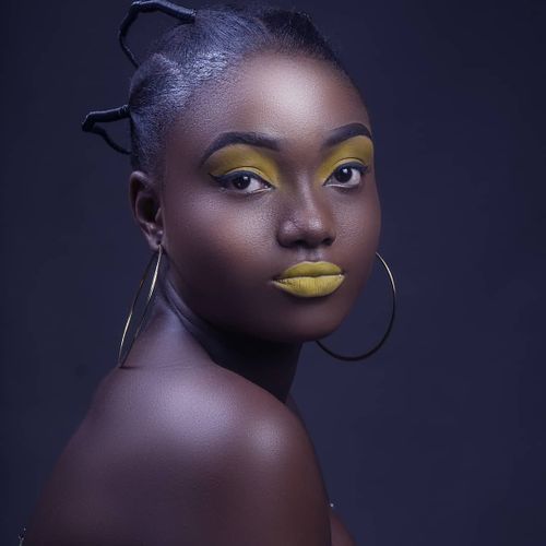 Free Striking studio portrait of a woman with bold yellow makeup and stylish hoop earrings on a dark background. Stock Photo