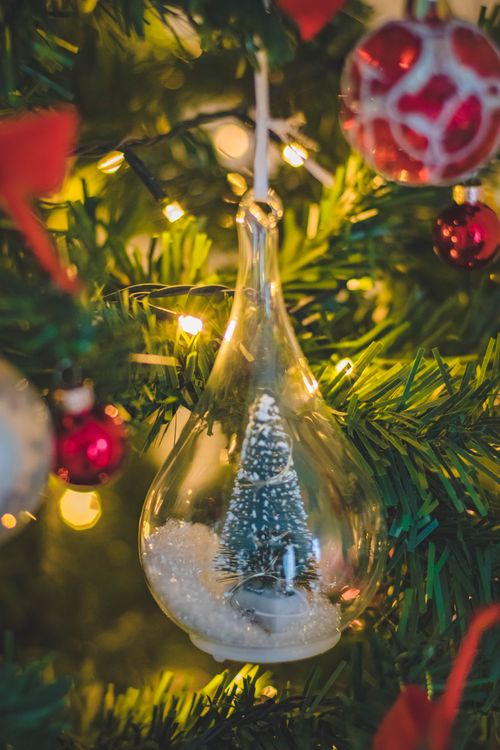 Free Delicate Christmas ornament hanging on a beautifully lit evergreen tree, adorned with festive lights. Stock Photo