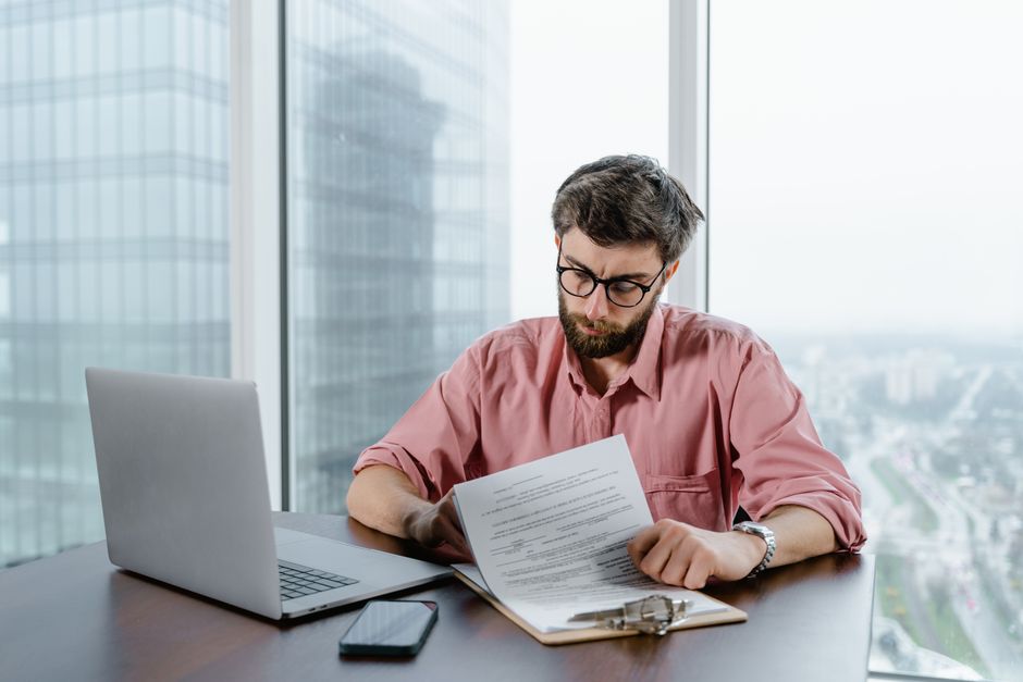 Hombre profesional en camisa rosa trabajando con documentos en un escritorio moderno.