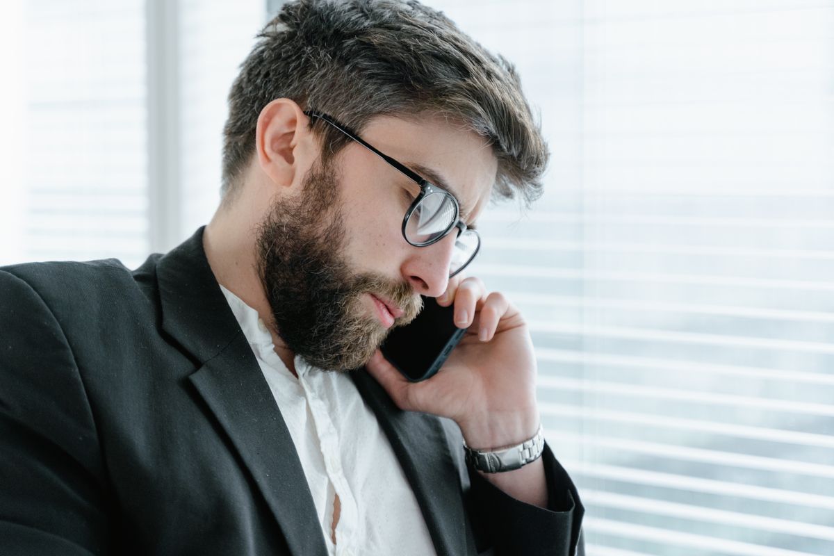 A bearded businessman in a formal suit engaged in a phone call indoors