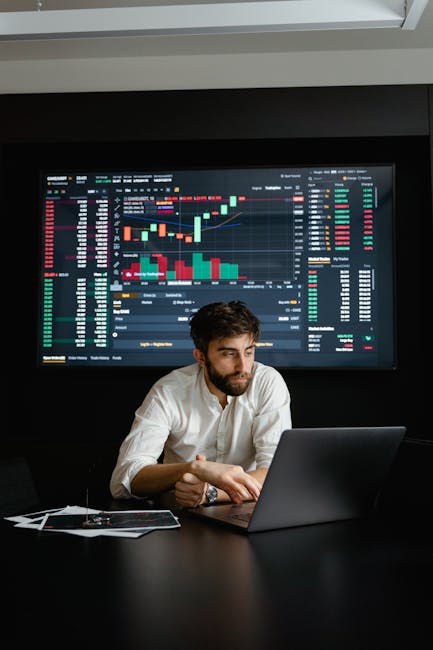 A man analyzing stock market data on a laptop in an office setting with a projector screen displaying financial charts. A man analyzing stock market data on a laptop in an office setting with a projector screen displaying financial charts.