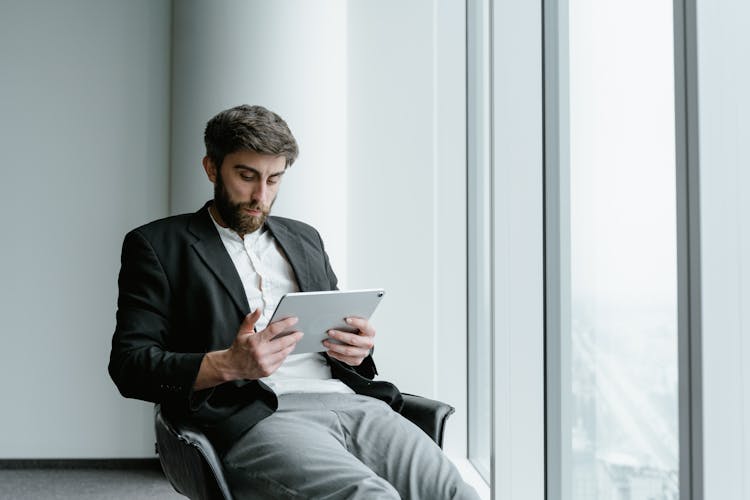 A Man In Black Coat Using A Tablet