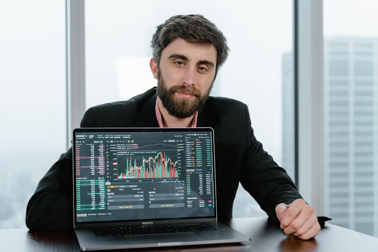 A Man In Black Coat Sitting Behind A Laptop