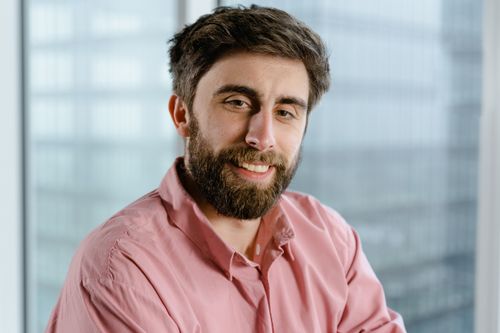 Free Close-up portrait of a smiling man with a beard in a pink shirt. Professional setting. Stock Photo