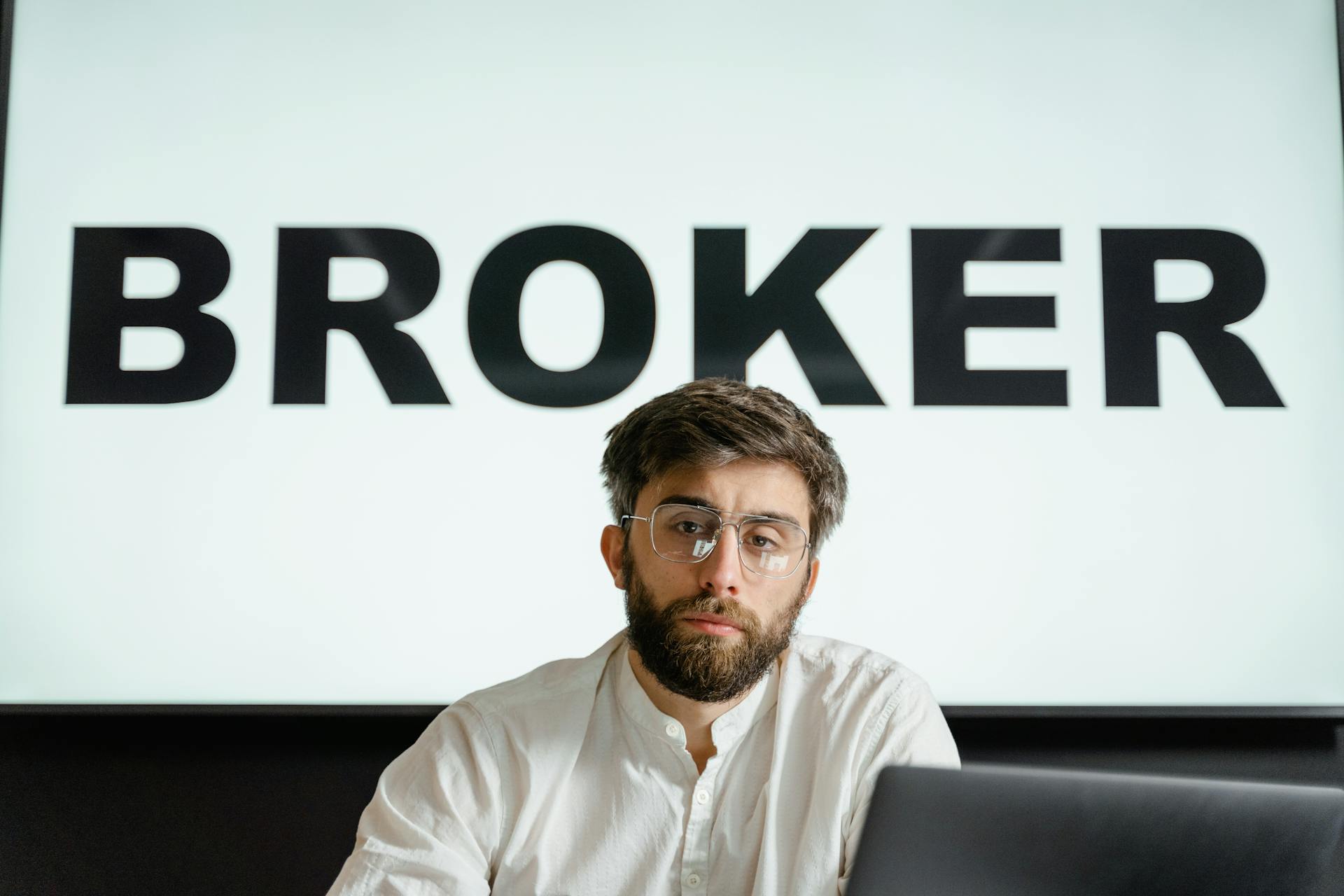 Portrait of a confident businessman sitting in an office under the sign 'BROKER'.