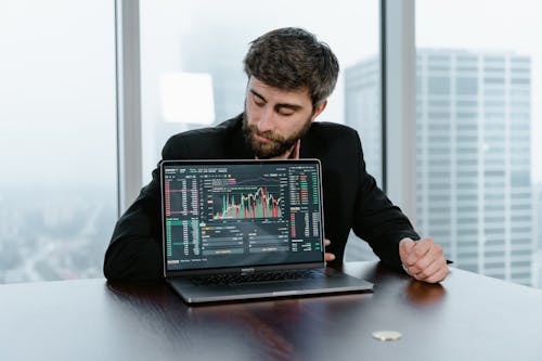 A Man in Black Suit Looking at the Laptop on the Table