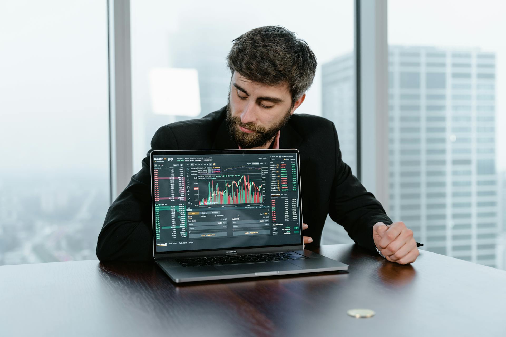 Focused trader examines stock market graphs on laptop in office setting.