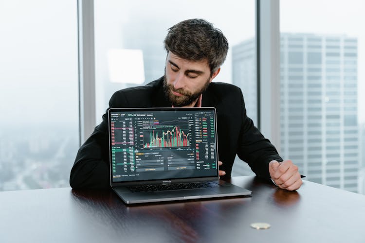 A Man In Black Suit Looking At The Laptop On The Table