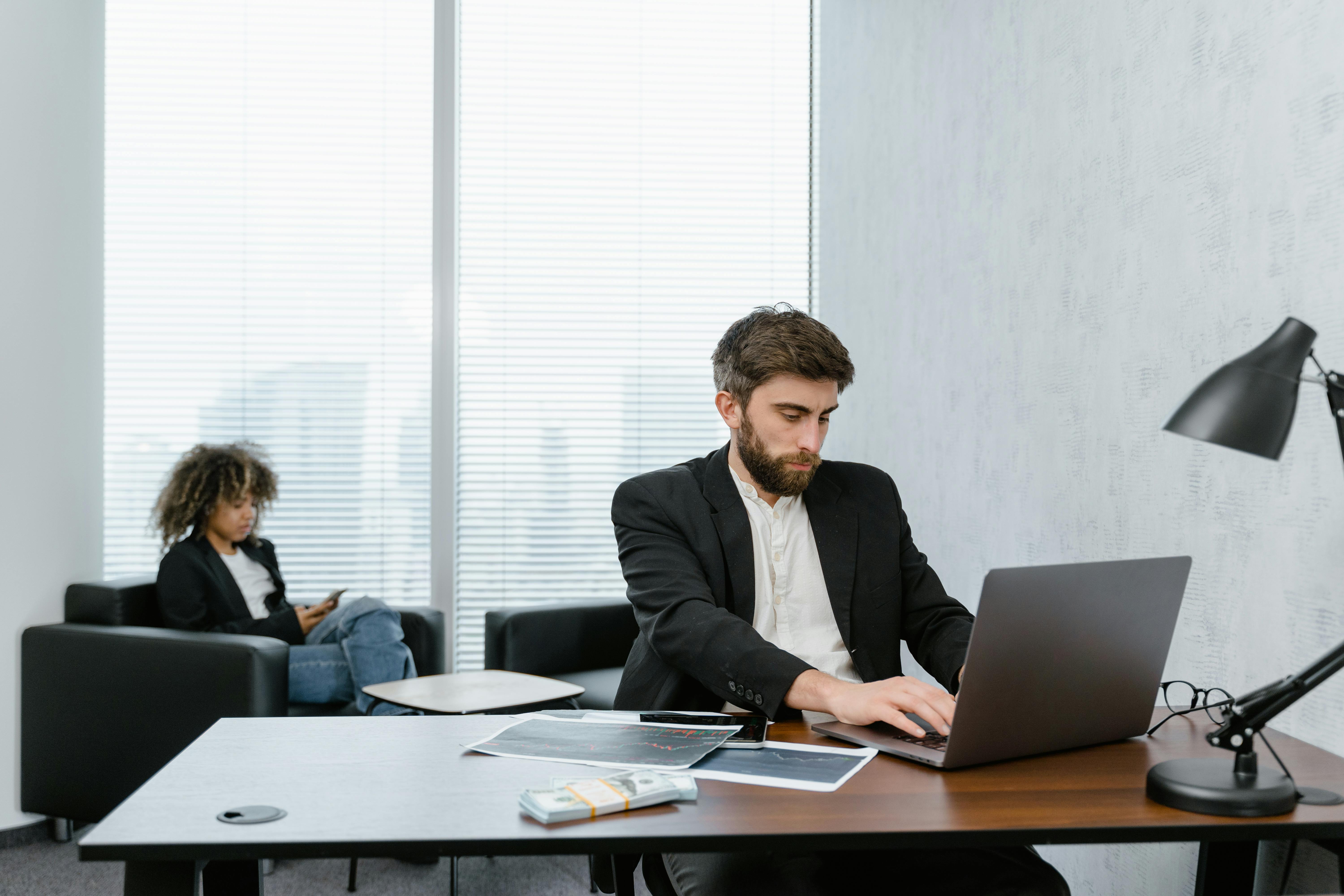 man in black suit jacket sitting on chair in front of laptop computer