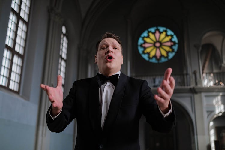 Choir Conductor In Black Suit Jacket With Bowtie Doing A Hand Signal With Mouth Open