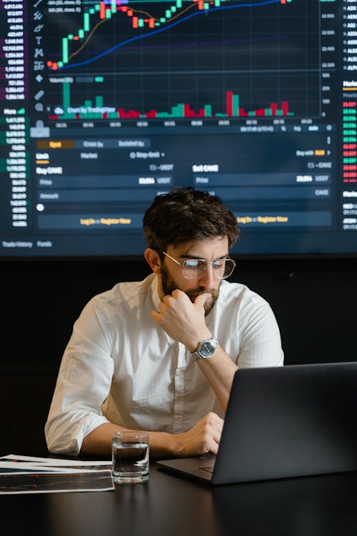 Bearded Man in White Dress Shirt Wearing Eyeglasses Sitting in Front of Laptop Feeling Pensive