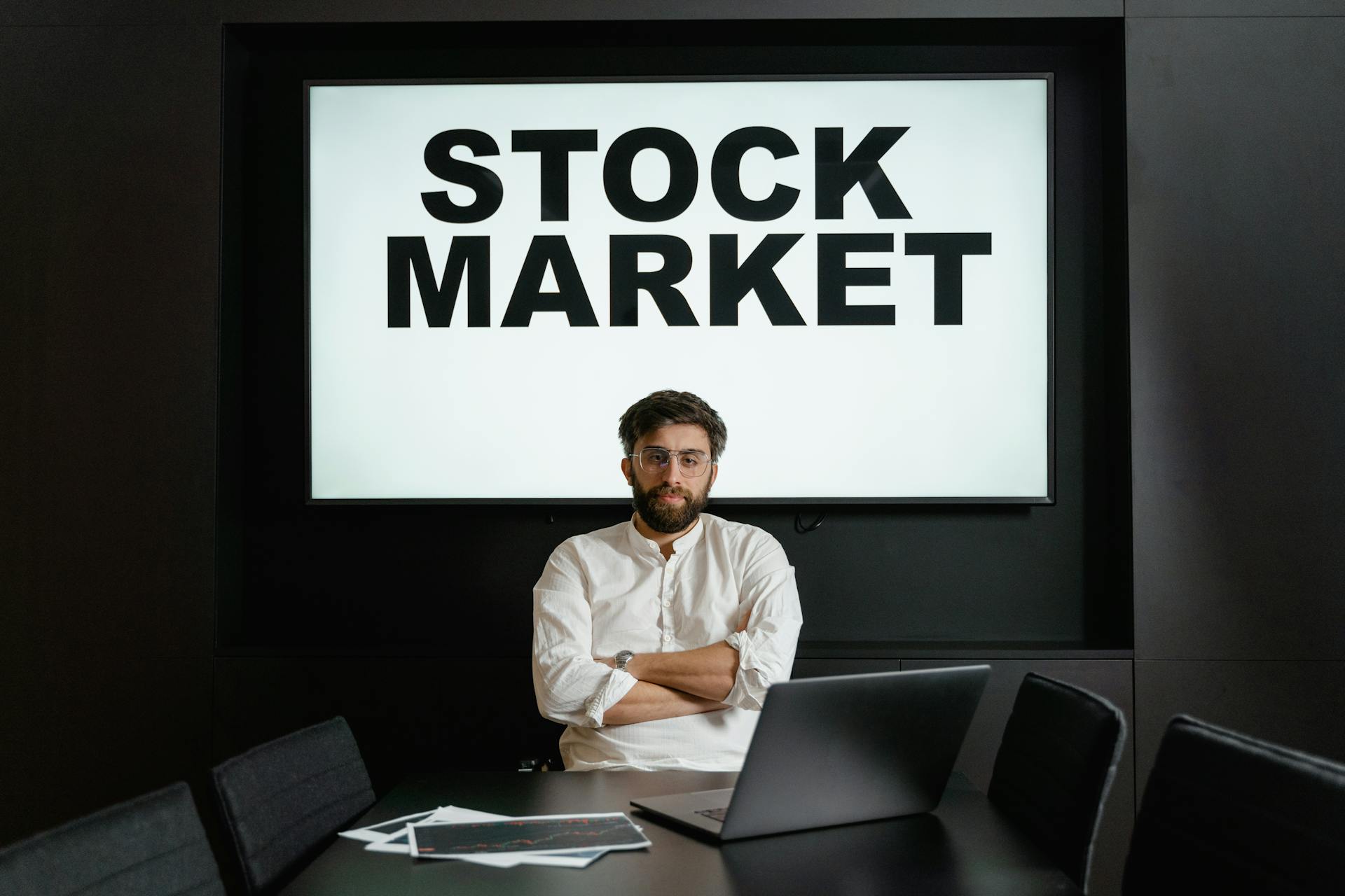 Big Screen with Stock Market Text on Display Behind a Man in White Dress Shirt