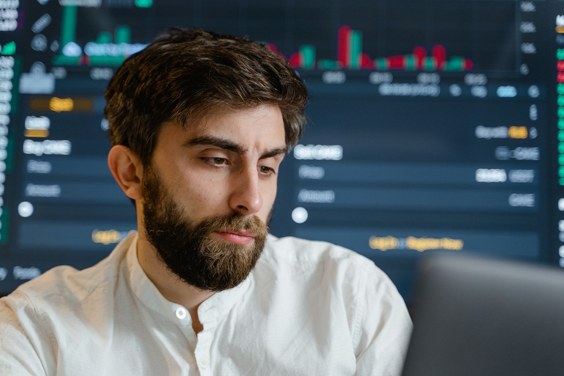 Close-up of thoughtful businessman with beard analyzing stock market data on screen.
