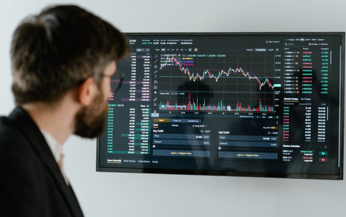 A businessman in a suit looks at a screen displaying stock market charts and data analysis.