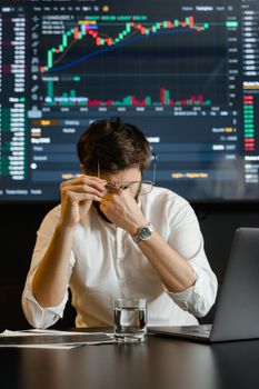 Tired businessman looking at stock charts on a laptop, feeling stressed.