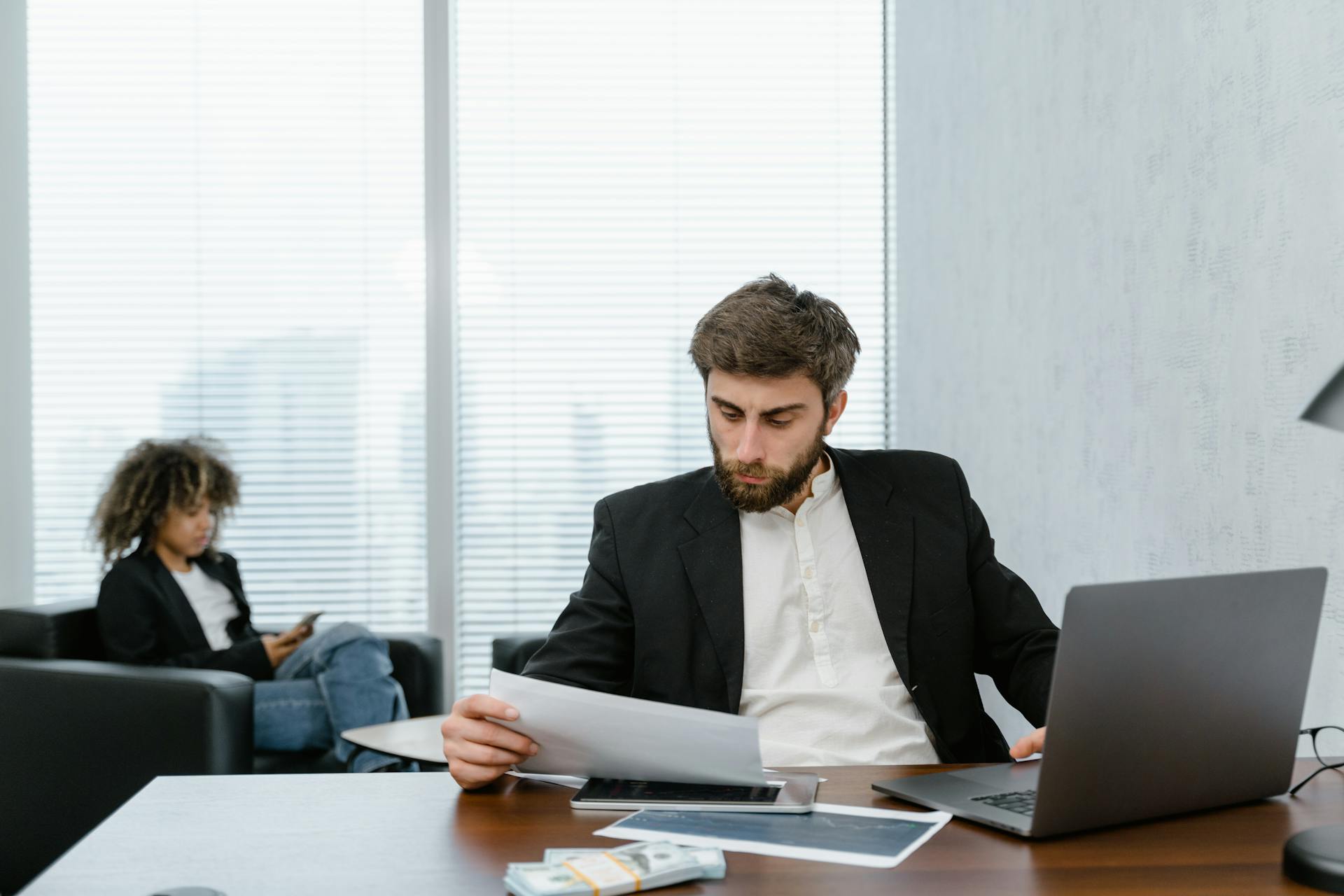 Focused businessman reviews financial reports at office desk with laptop.