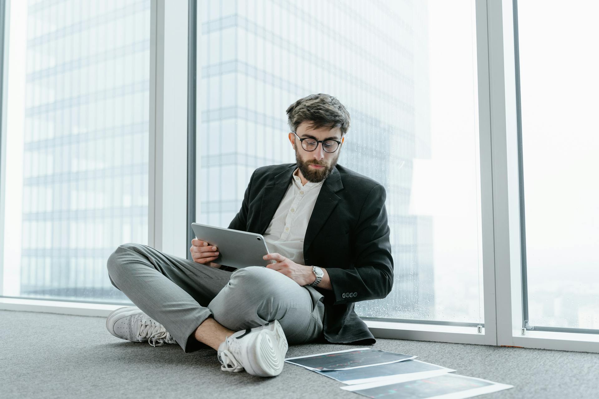 Young businessman with glasses using a tablet in a modern office setting.