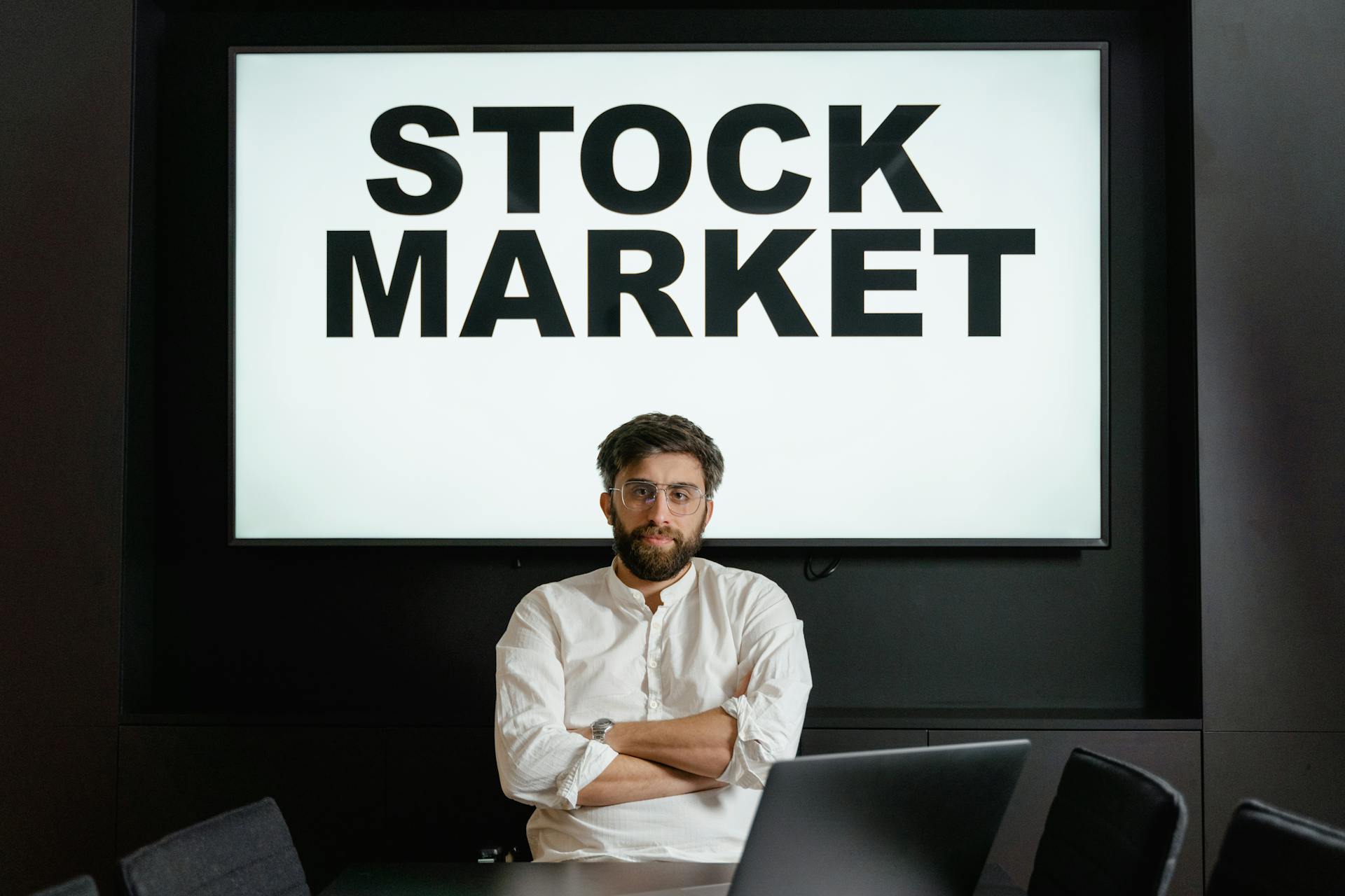 Confident businessman sitting in front of a stock market display screen in a modern office setting.