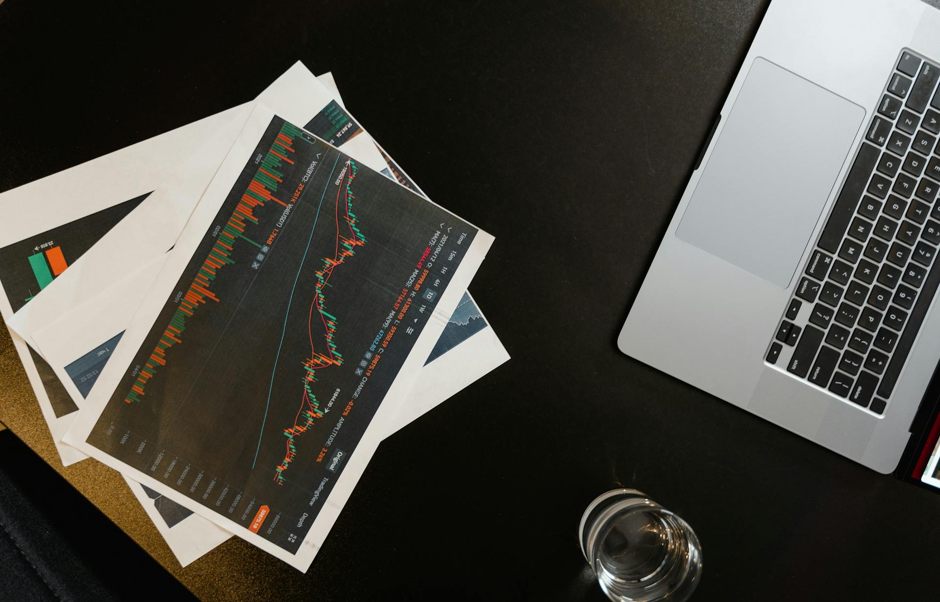 An overhead view of charts and graphs alongside a laptop on a black surface.