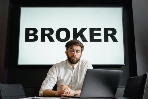 Free A broker with glasses sits confidently in front of a laptop in a modern conference room. Stock Photo