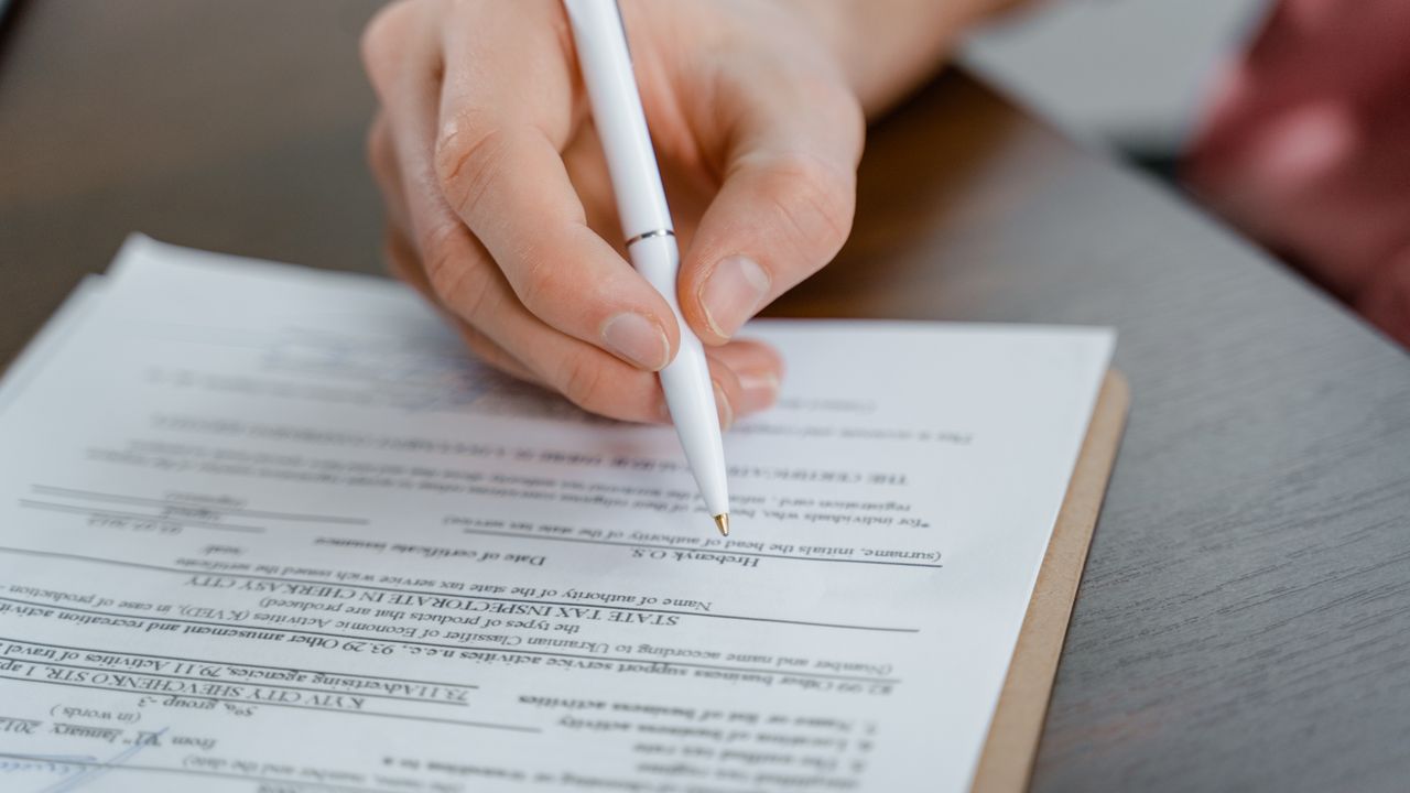 A hand holding a pen signing a document, close-up shot with focus on the paper.