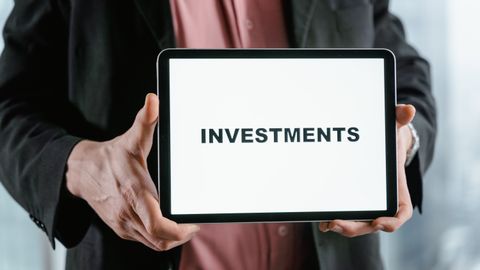 A businessman in a suit holds a tablet displaying the text 'INVESTMENTS'.