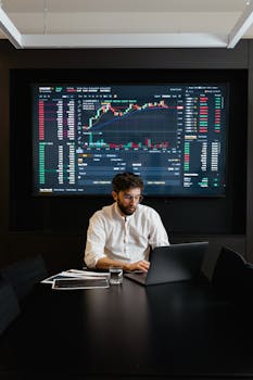 A stock trader analyzes cryptocurrency data on a laptop with graphs and charts on a screen.