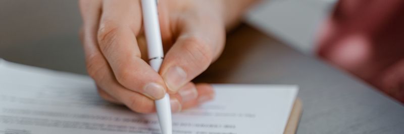 Detailed view of a hand writing a signature on an official document with a ballpoint pen.