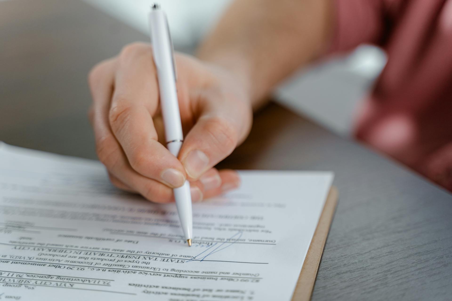 Detailed view of a hand writing a signature on an official document with a ballpoint pen.